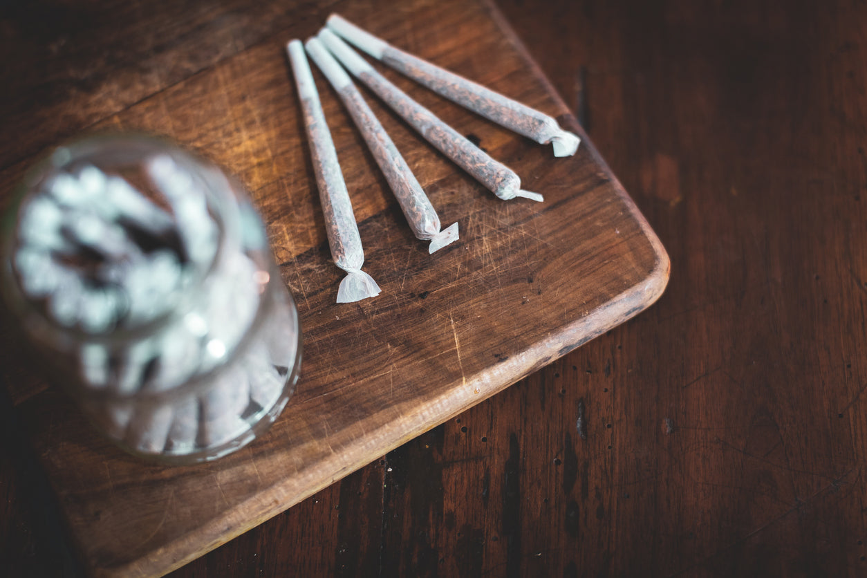 Four filled pre-rolled cones on a wooden cutting board, with a jar of cones blurred in the foreground.