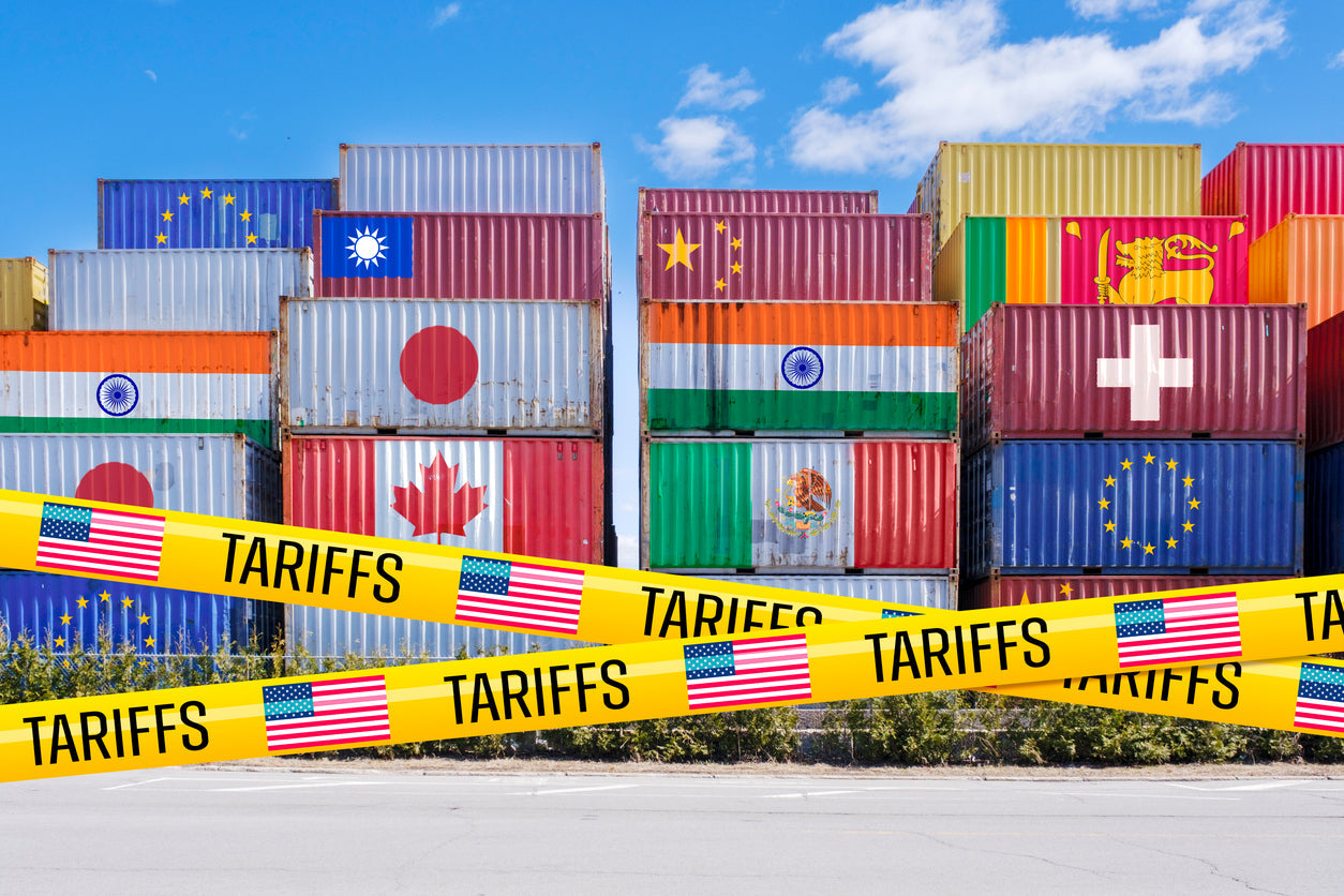 Shipping containers painted with country flags behind yellow “TARIFFS” tape with U.S. flags, symbolizing global trade restrictions.