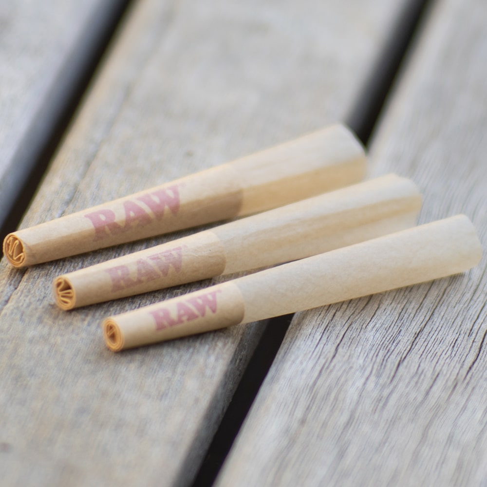 Three RAW dogwalker pre rolled cones with different filter lengths rest on a wooden surface